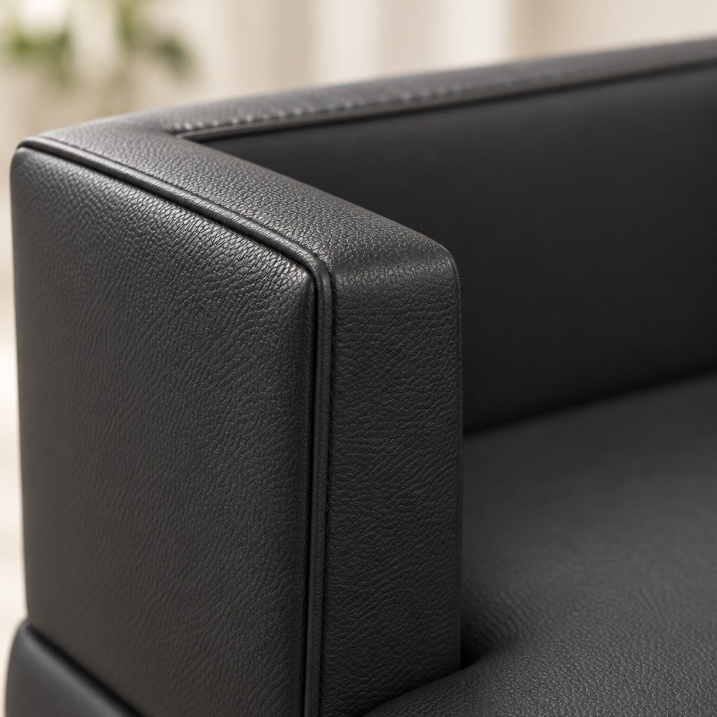 Gros plan sur l'angle haut d'un accoudoir de la banquette en simili noir, la surpiqûre de bordure et le grain fin du revêtement bien lisibles.