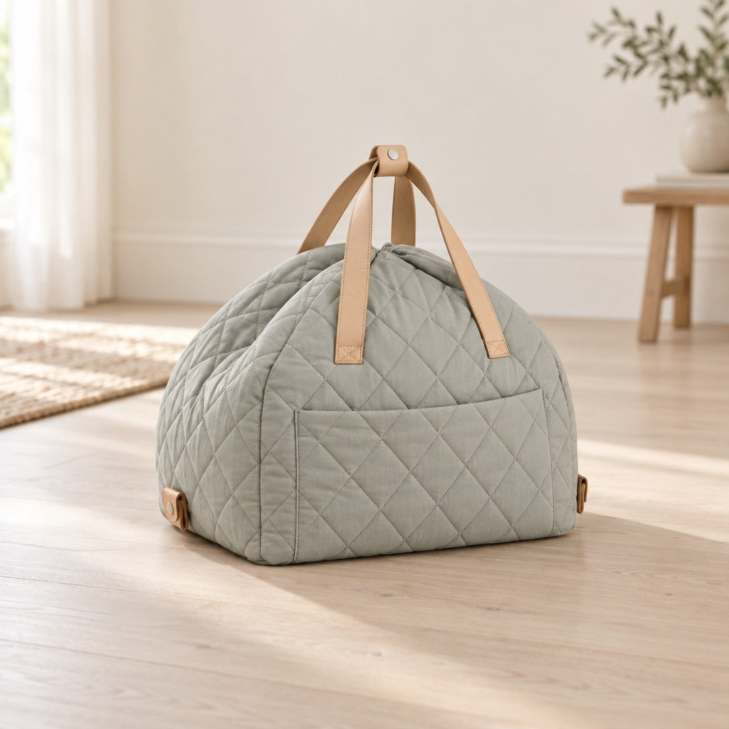 La cabine gris sauge pâle seule et fermée sur un parquet clair, en dôme matelassé, ses deux anses de cuir réunies au sommet et sa poche plaquée bien visible.