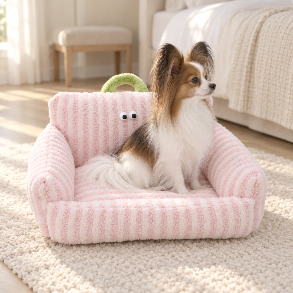 Epagneul papillon blanc et zibeline assis de profil dans le couchage canape en peluche rayee rose dragee, sur un tapis de laine.