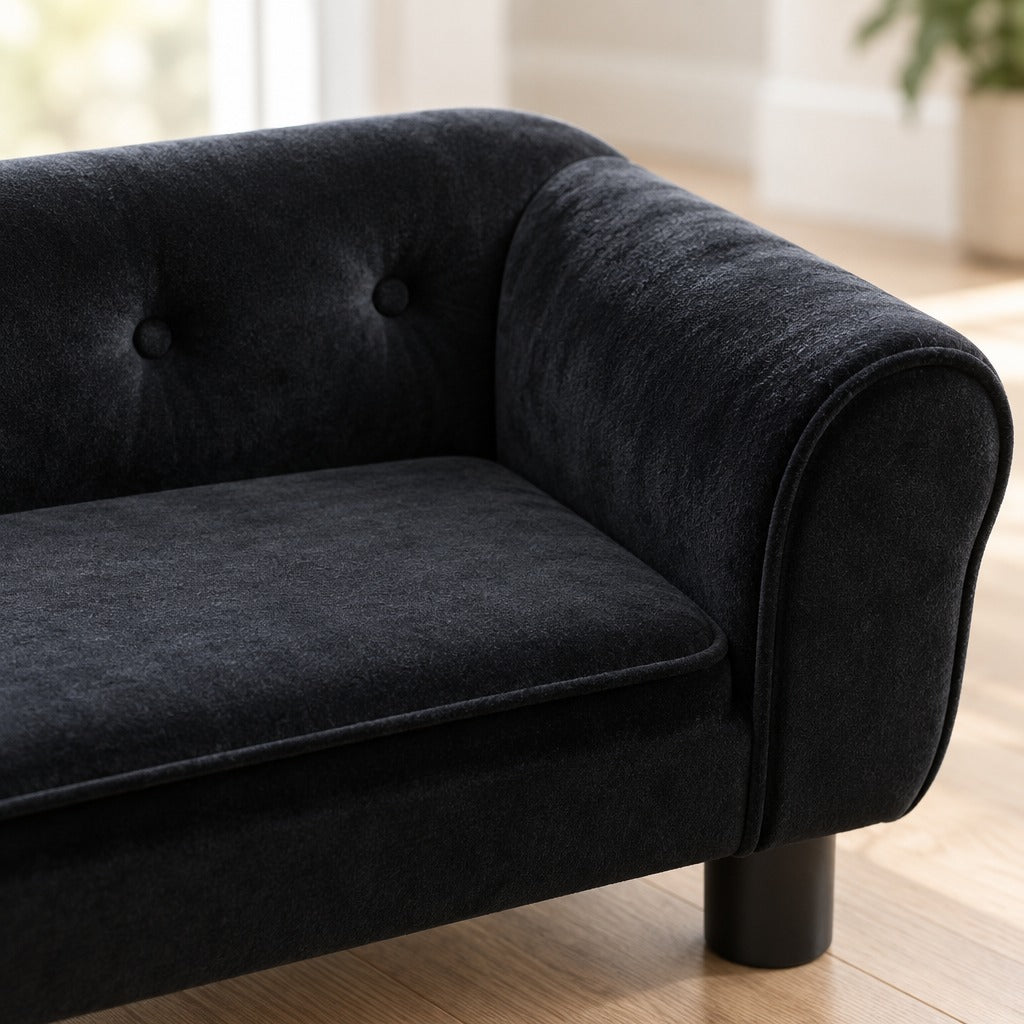 Gros plan sur le velours noir à poil ras du dossier capitonné et de l'accoudoir roulé du canapé, sans animal.
