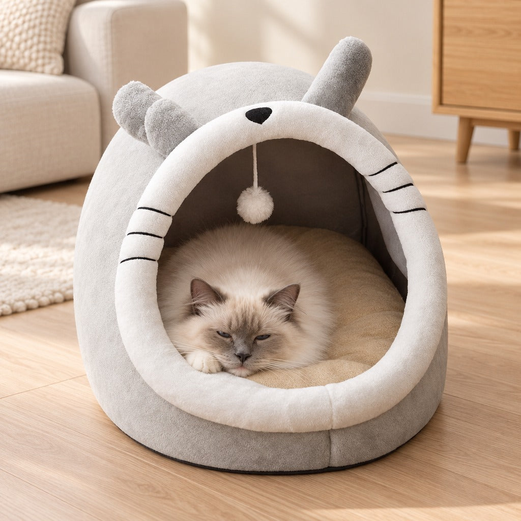 Chat sacré de Birmanie assoupi dans le cocon gris perle posé sur un parquet clair.