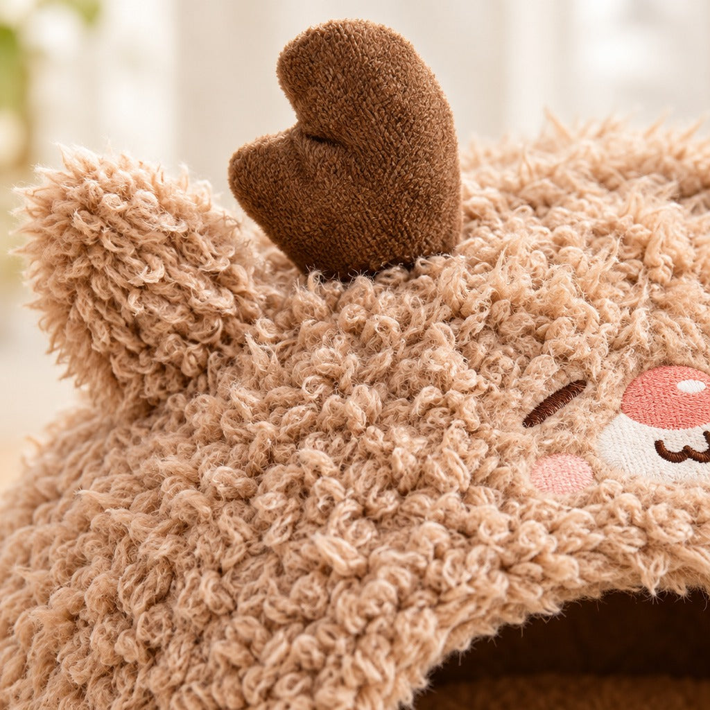 Gros plan sur la peluche bouclée du cocon beige renne, une oreille et la base d'un bois de cerf au bord du cadre.