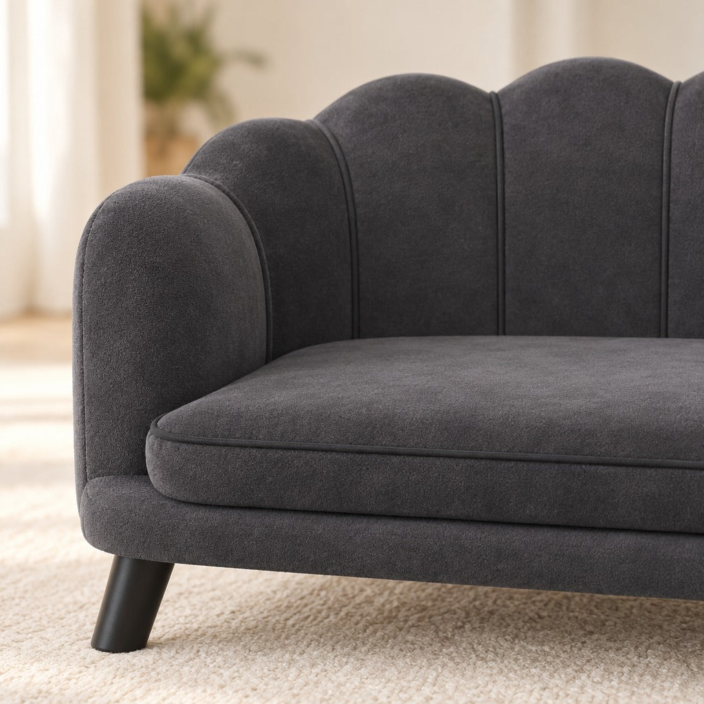 Gros plan sur le velours gris anthracite du dossier en coquille, les coutures verticales des lobes et l'accoudoir rond bien lisibles.