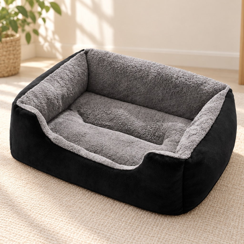 Corbeille moelleuse noire posée seule sur un tapis clair, peluche grise à l'intérieur et suédine noire à l'extérieur.