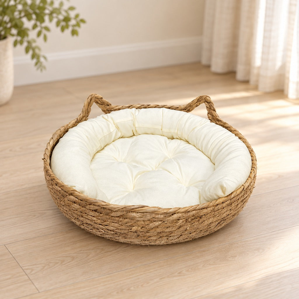 Corbeille pour chat en fibre végétale tressée posée seule sur un parquet clair, avec son coussin écru uni.