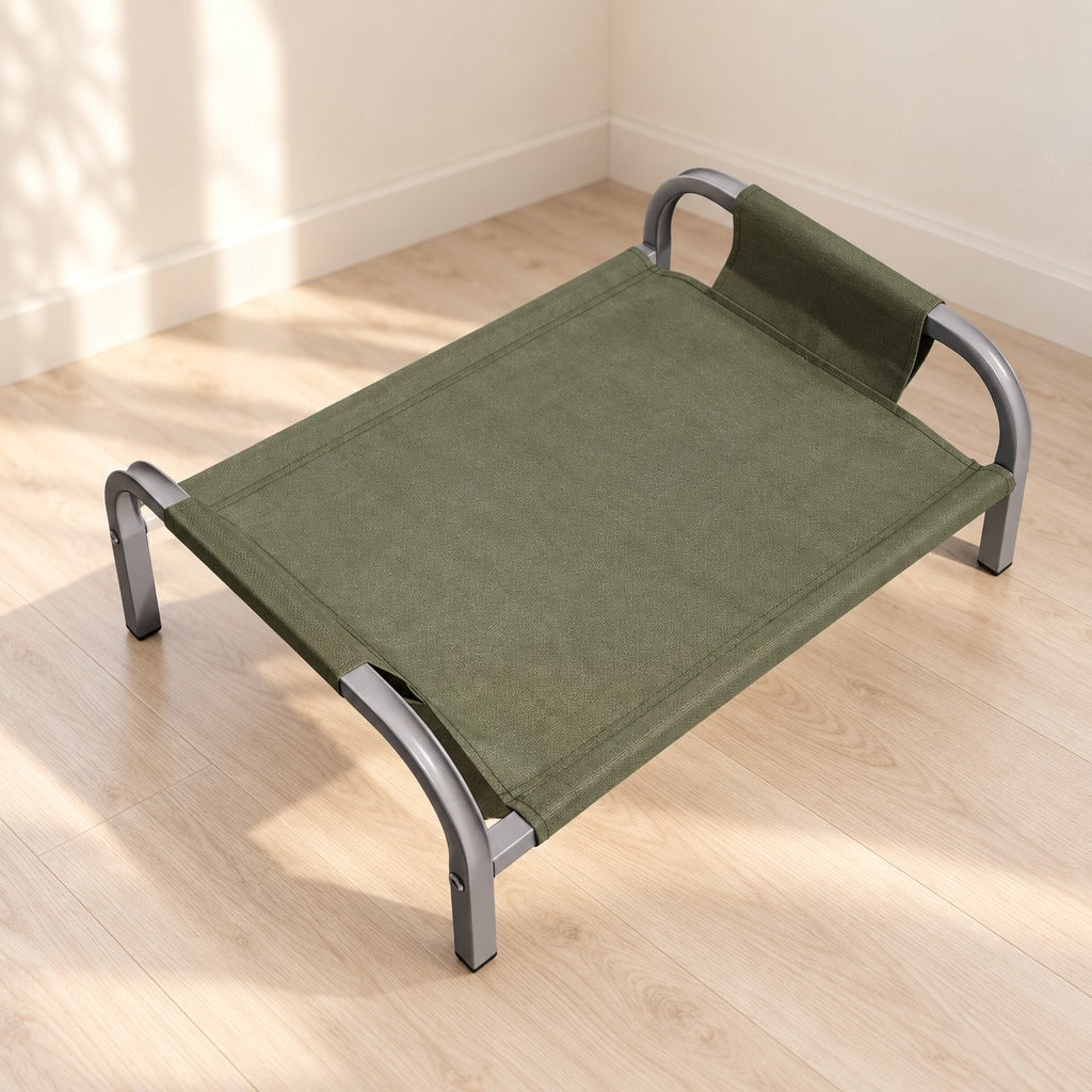 Le couchage surélevé vert kaki seul dans un angle de pièce clair, sa toile tendue, son dossier relevé à une extrémité et ses quatre pieds cintrés.
