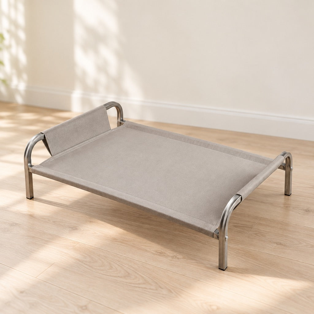 Le couchage surélevé gris clair seul sur un parquet blond devant un mur crème, vu de trois quarts depuis son extrémité ouverte.