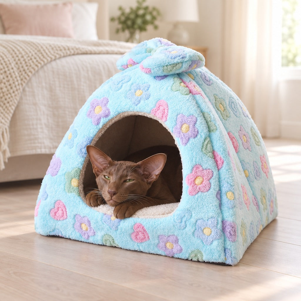 Un chat oriental brun havane somnole dans l'ouverture du dôme en peluche bleu fleuri, au pied d'un lit.