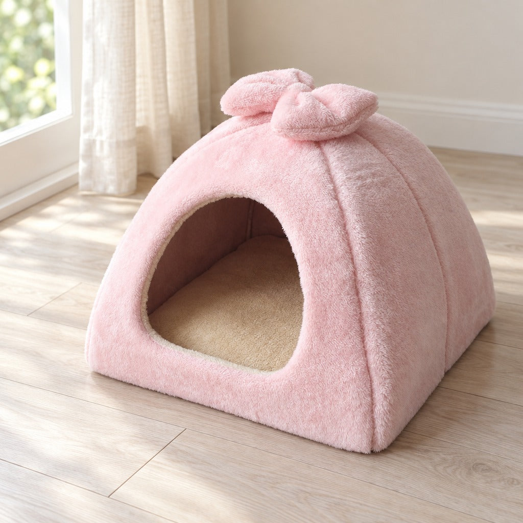 Le dôme en peluche rose poudré posé près d'une fenêtre, nœud au sommet, arche unique et coussin beige au fond.