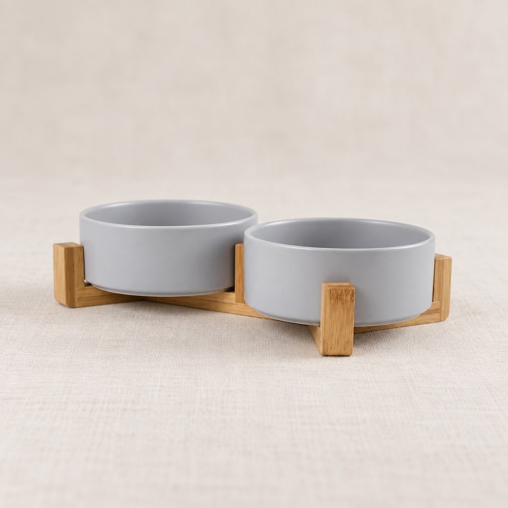 Duo de bols gris clair dans son socle de bois clair, seul sur un fond clair, vu de trois quarts.