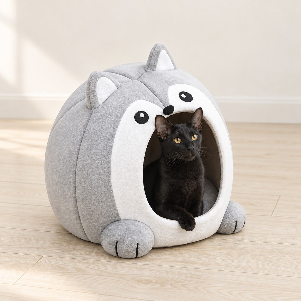 Un chat noir assis à l'entrée de la maison caverne gris perle, une patte avant posée sur le rebord blanc, dans un salon au parquet clair.