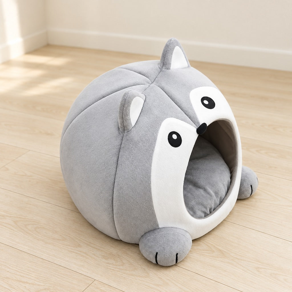 La maison caverne gris perle pour chat, seule sur un parquet clair, vue de trois quarts, son coussin rond posé au fond.