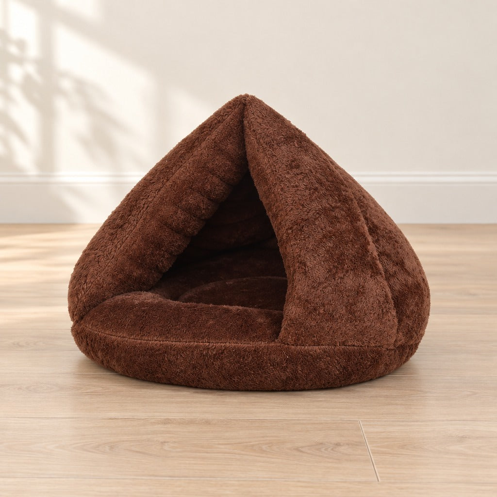 Nid cabane pour chat en peluche chocolat posé seul sur un parquet clair, entrée triangulaire face à l'objectif.
