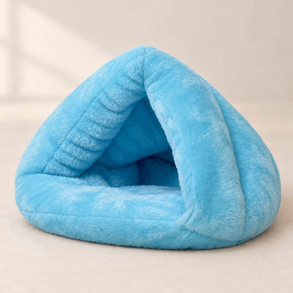 Nid cabane pour chat en peluche bleu ciel posé seul sur une surface claire, entrée triangulaire ouverte sous la pointe.