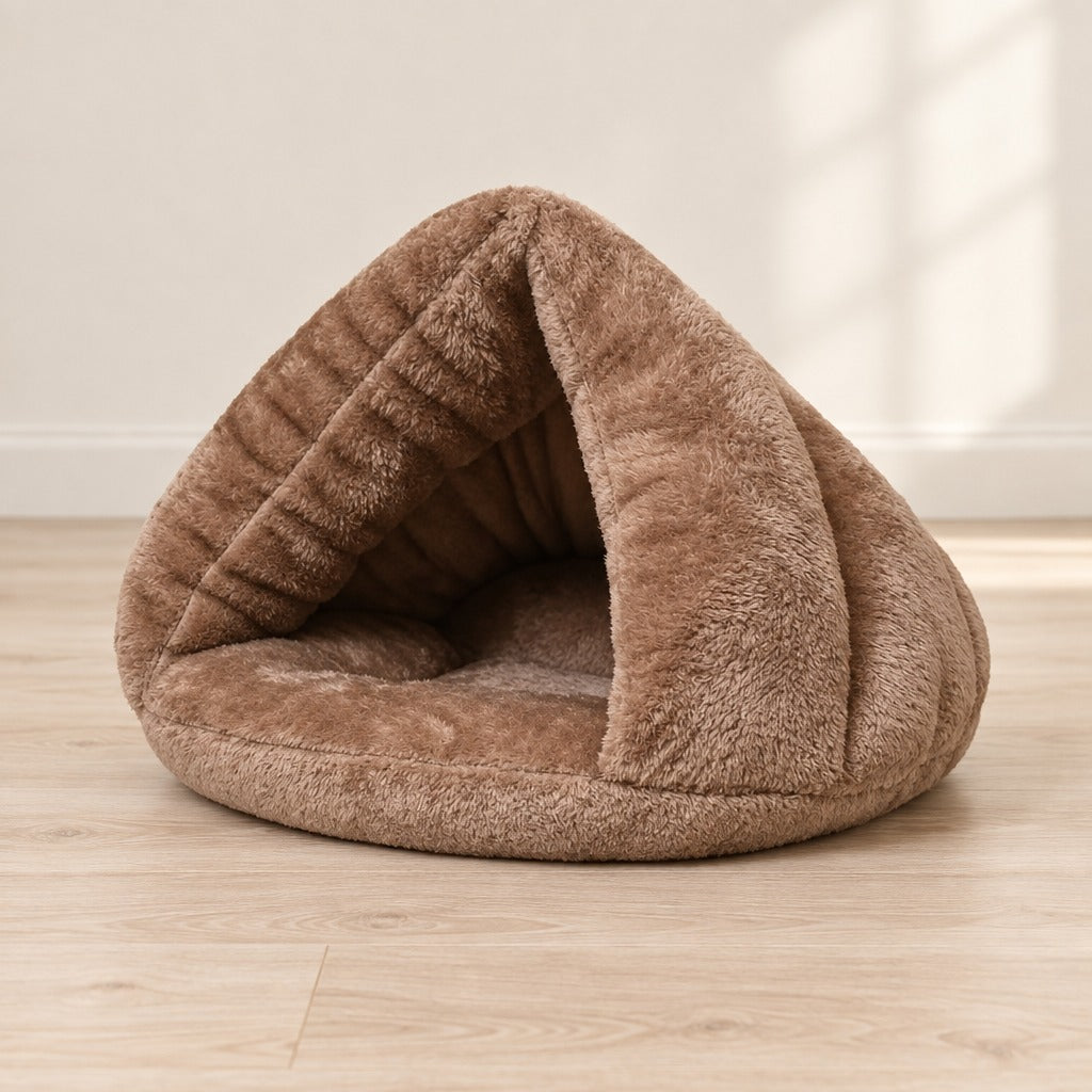 Nid cabane pour chat en peluche taupe posé seul sur un parquet clair devant un mur crème.