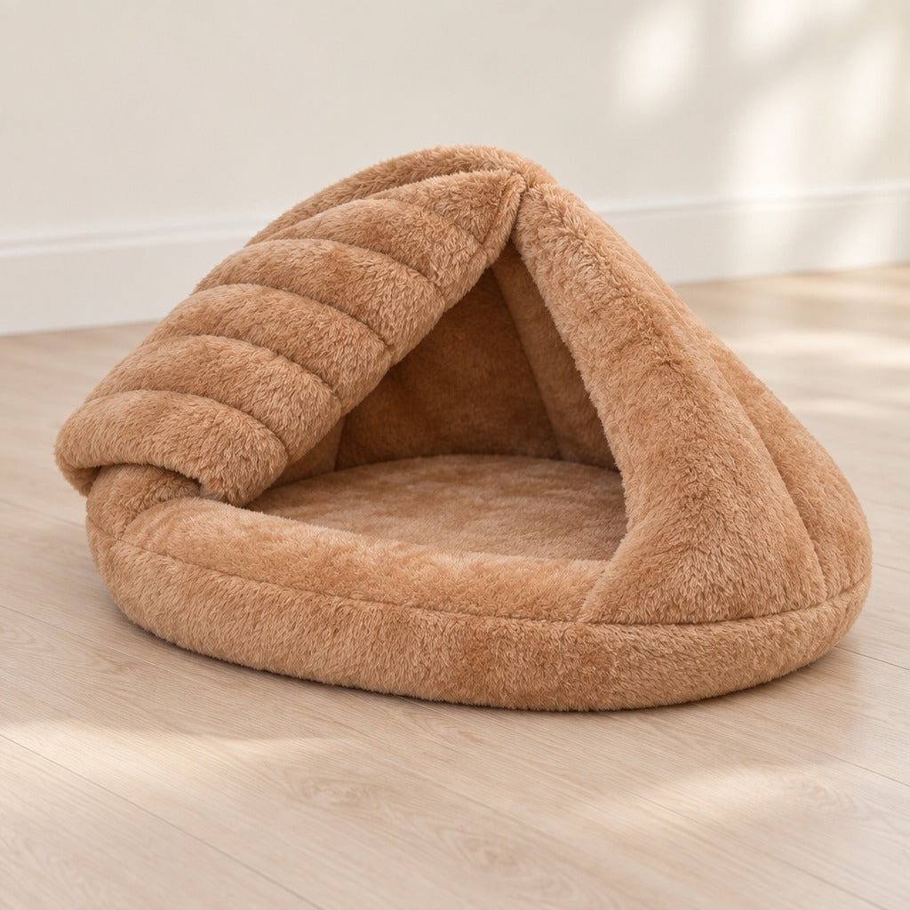 Nid cabane pour chat en peluche caramel posé seul sur un parquet clair, un pan de toit rabattu qui découvre l'assise.