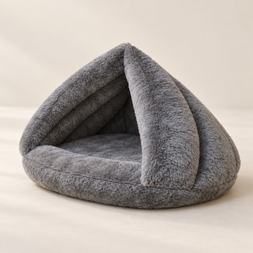 Nid cabane pour chat en peluche gris posé seul sur une surface claire, les deux pans du toit écartés.