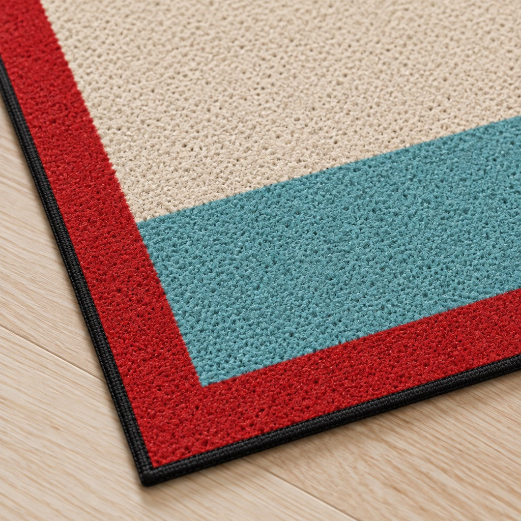 Gros plan sur un angle du paillasson crème, turquoise et rouge, sa bordure rouge, sa fine ganse sombre et son relief granuleux.