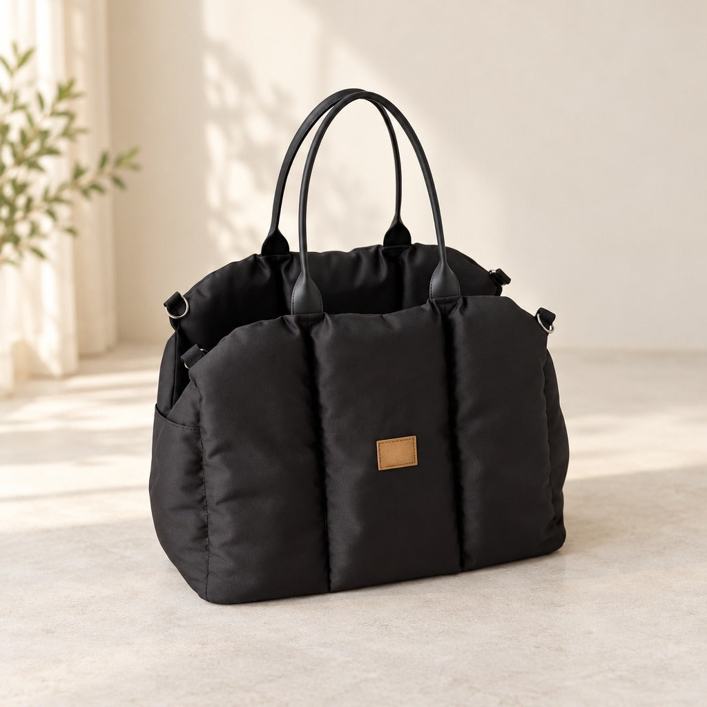 Sac de transport matelassé noir seul, vu de trois quarts sur fond clair, avec ses deux anses et sa poche plaquée.