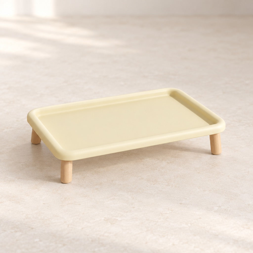 Le plateau repas surélevé jaune vanille seul et vide sur fond clair, vu de trois quarts, bord relevé continu et quatre pieds en bois.
