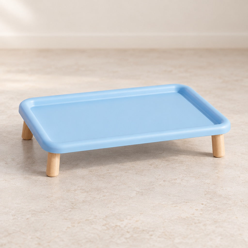 Le plateau repas surélevé bleu ciel seul et vide sur fond clair, vu de trois quarts, bord relevé continu et quatre pieds en bois.
