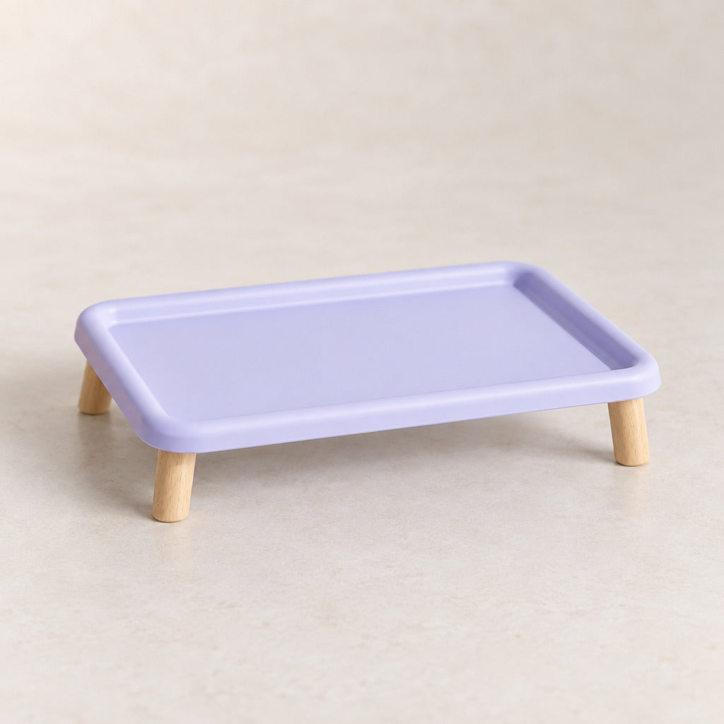 Le plateau repas surélevé lilas seul et vide sur fond clair, vu de trois quarts, bord relevé continu et quatre pieds en bois.