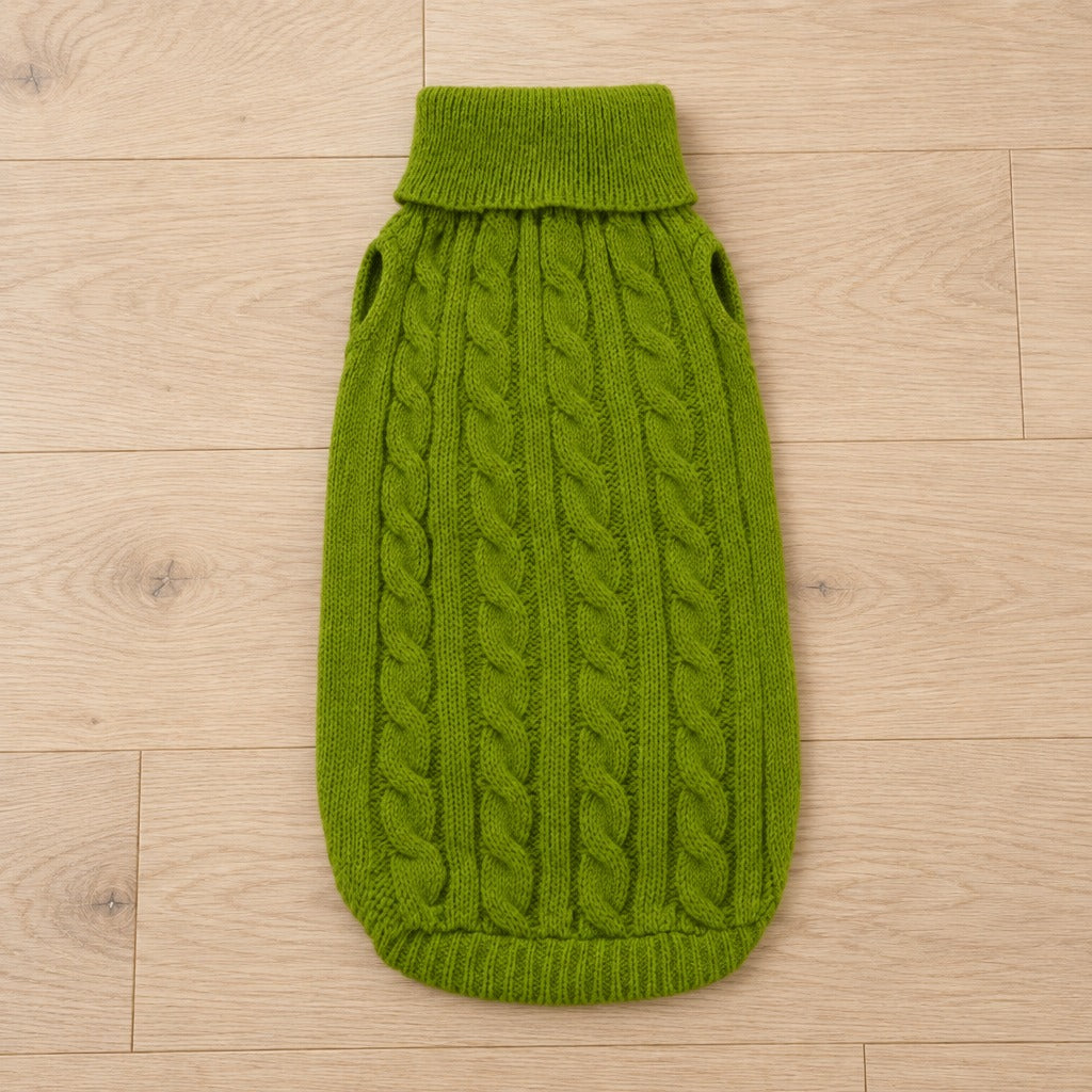 Le pull pour chien seul, à plat sur un parquet clair, coloris Vert olive, avec son panneau de torsades central.