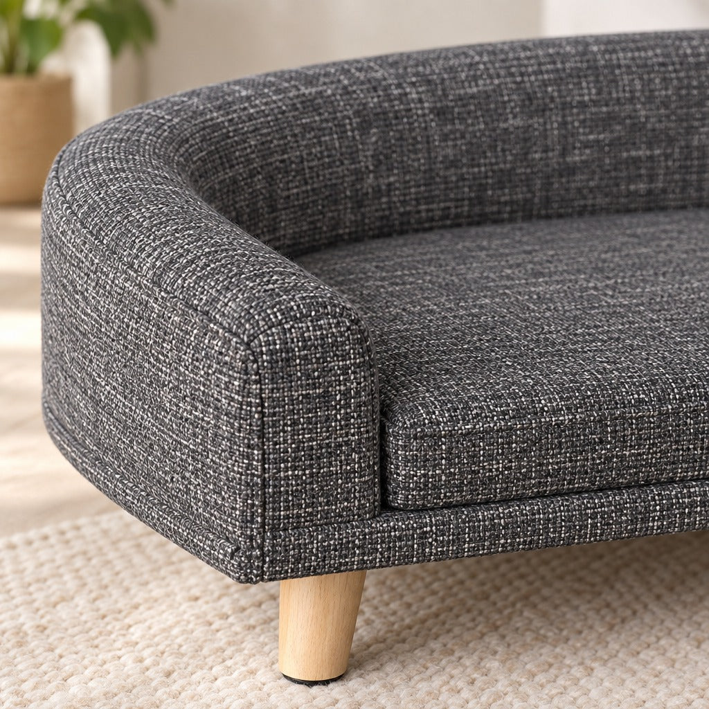 Gros plan sur l'accoudoir du sofa ardoise chiné, son tissu à grosse trame et un pied de bois clair.