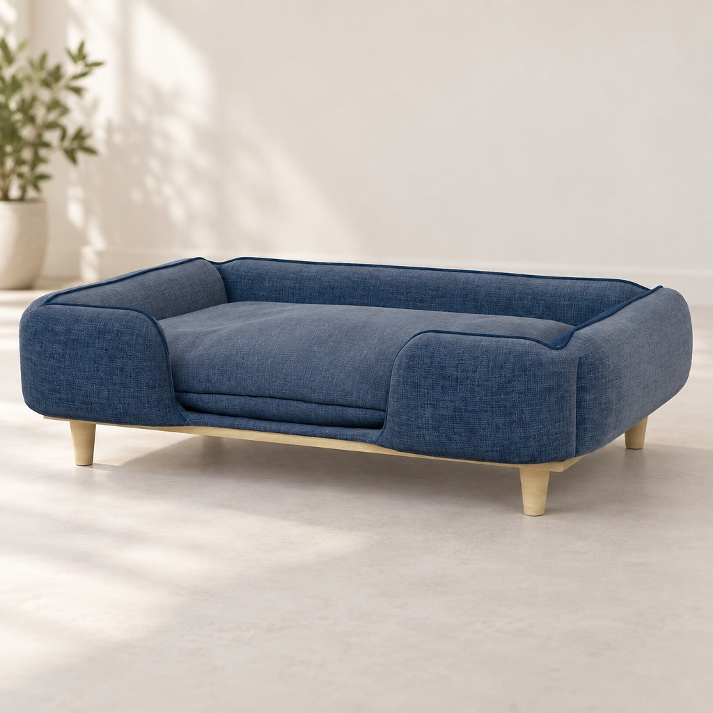 Le sofa pour chien bleu denim vu seul de trois quarts sur fond clair, son côté avant ouvert et ses quatre pieds coniques en bois clair.