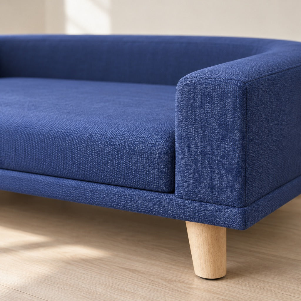 Gros plan sur le tissu tissé bleu nuit du sofa pour chien, sur l'extrémité droite de l'accoudoir et sur un pied conique en bois clair