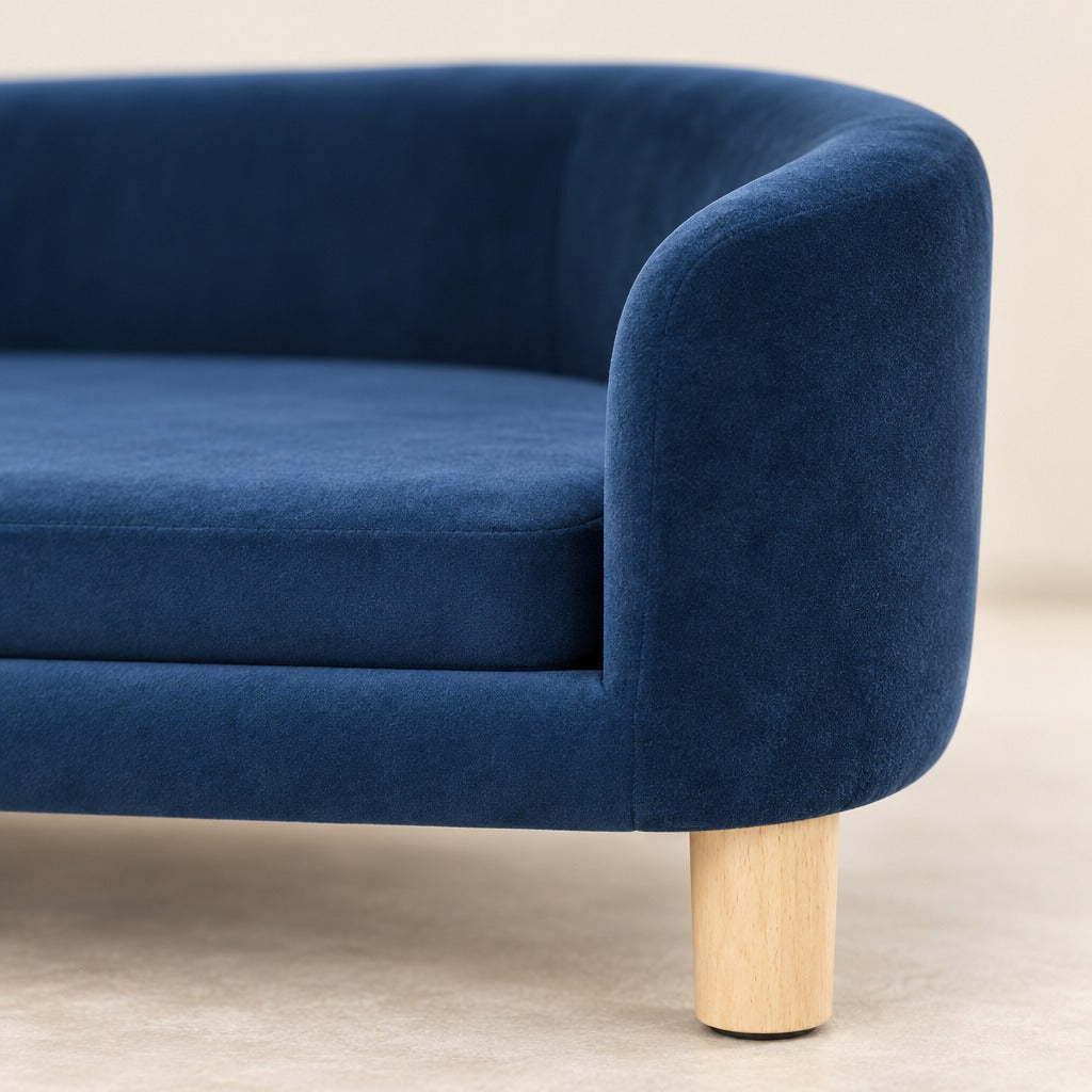 Gros plan sur le velours ras bleu nuit de l'accoudoir du sofa compact et sur un pied en bois clair.