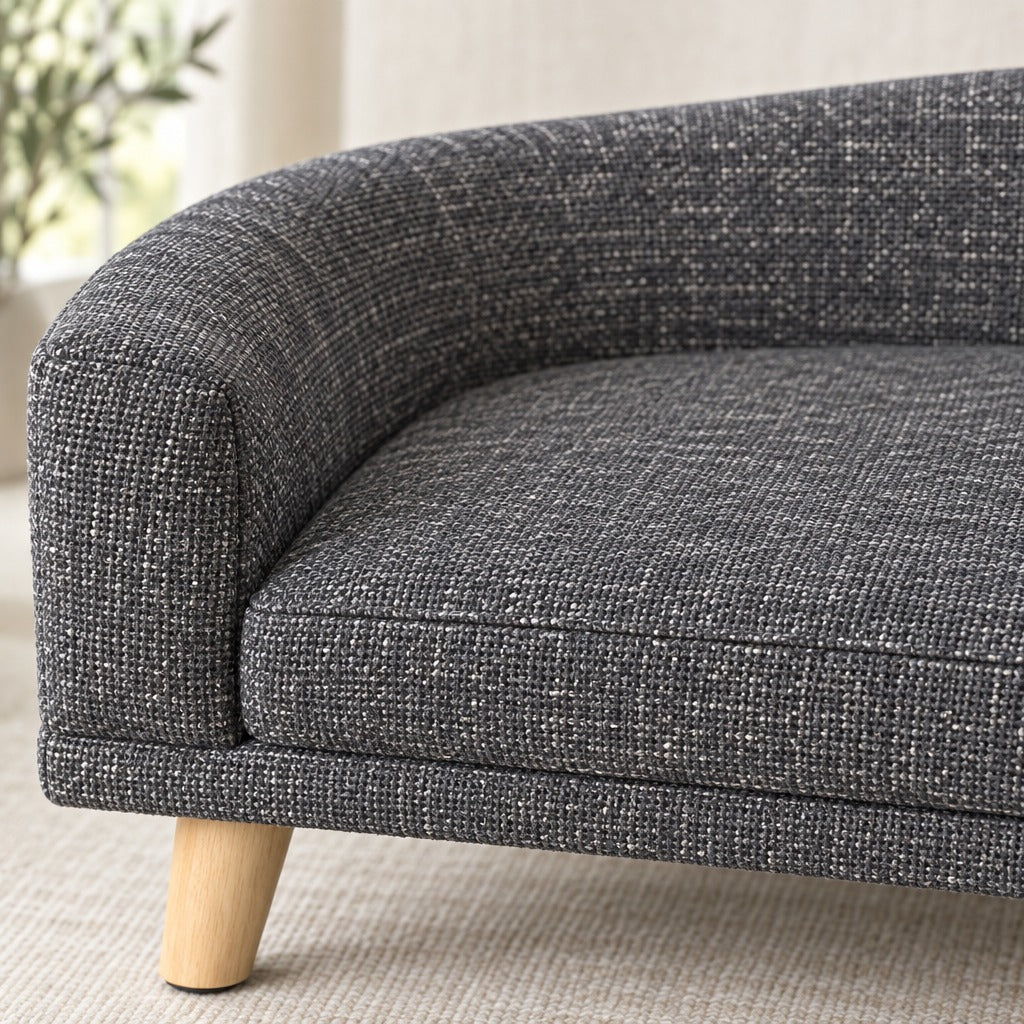 Gros plan sur l'accoudoir du sofa gris foncé, son tissu à grosse trame et un pied de bois clair.