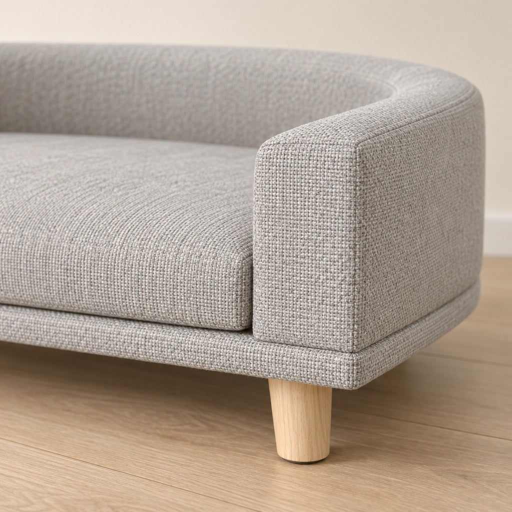 Gros plan de l'accoudoir de la banquette gris perle, trame du tissu et pied en bois clair.