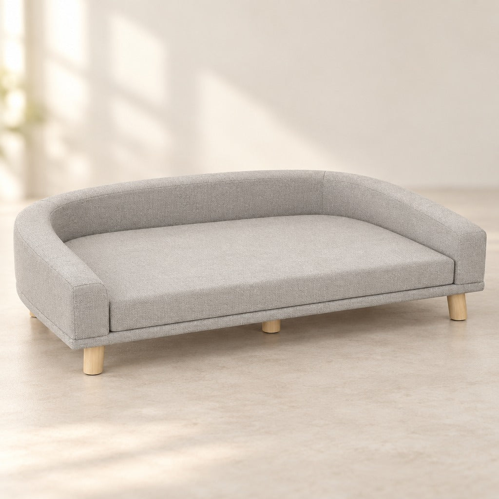 Le canapé pour chien gris clair vu seul de trois quarts sur fond clair, son bandeau continu, son coussin et ses quatre pieds en bois.