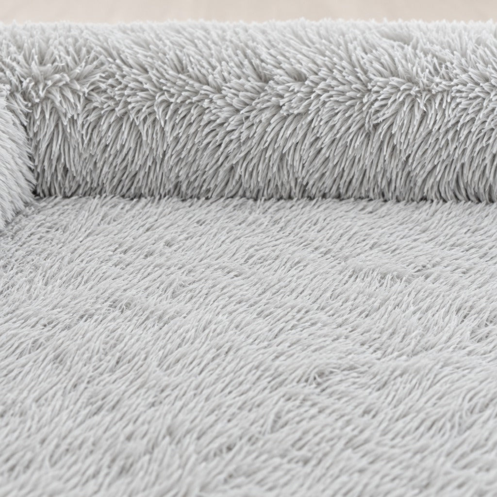 Gros plan sur les longues mèches de la peluche gris perle, du rebord arrière jusqu'à l'assise plate d'un seul tenant.