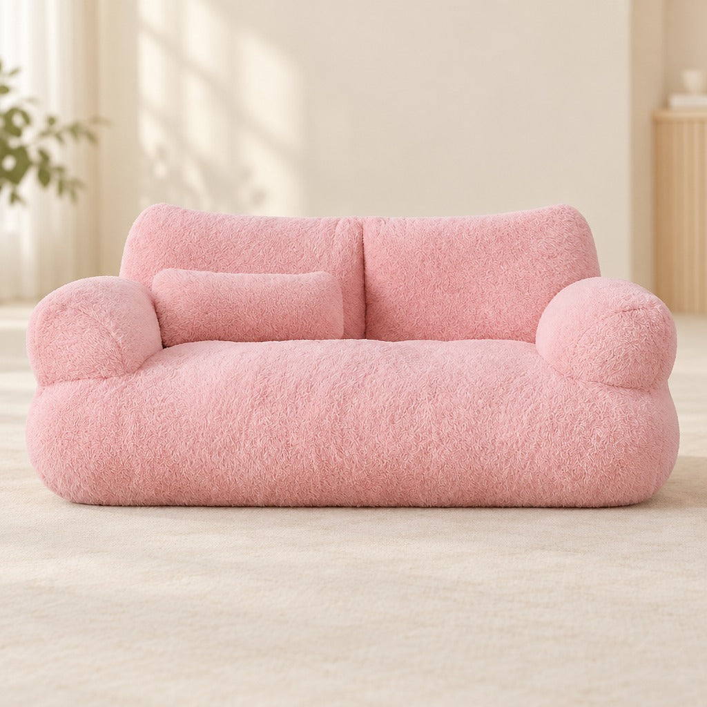 Le sofa moelleux rose poudré vu de face en entier, ses deux accoudoirs ronds et son traversin posé sur l'assise