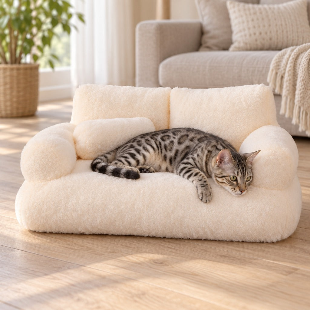 Un chat bengal tigré gris couché en travers de l'assise du sofa moelleux crème, la tête posée sur un accoudoir