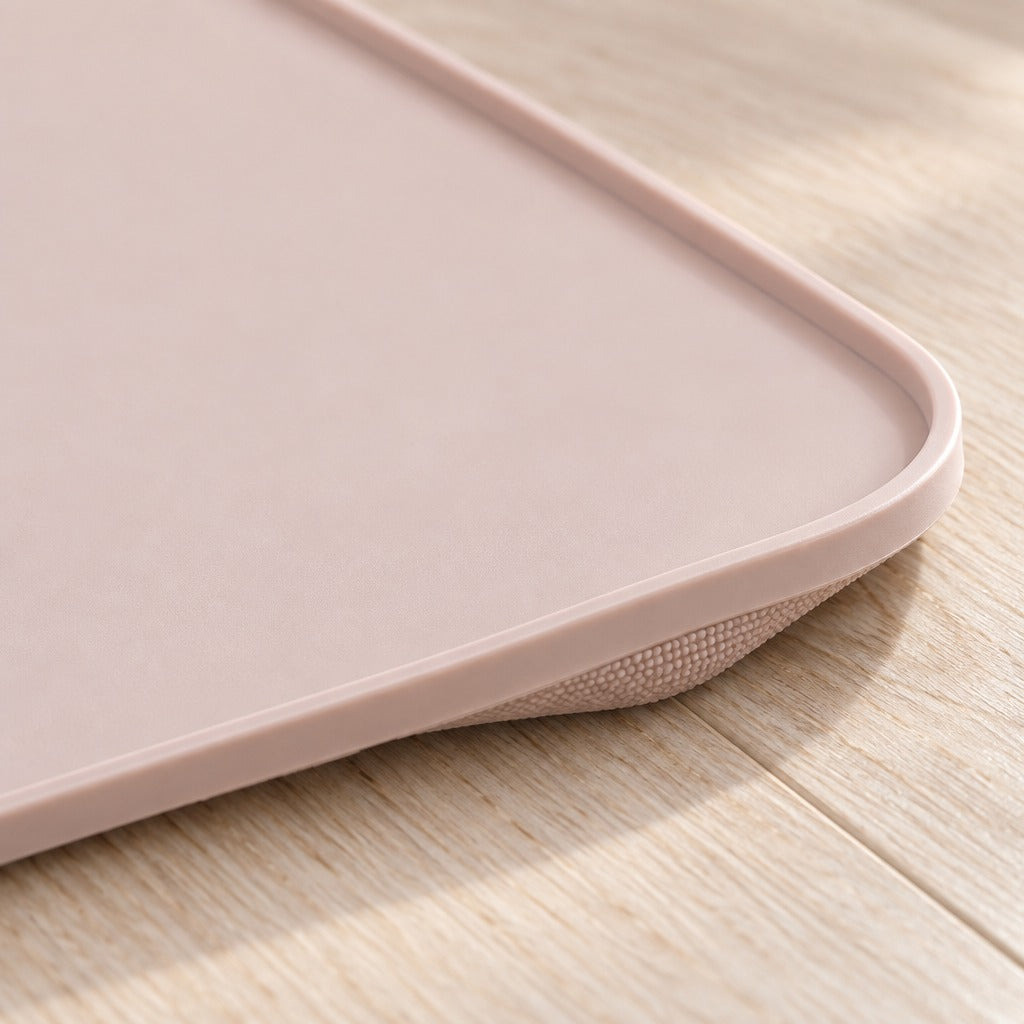 Gros plan sur un coin arrondi du tapis de gamelle pour chat rose poudré, avec son rebord bas continu et sa face grenée de fins picots.