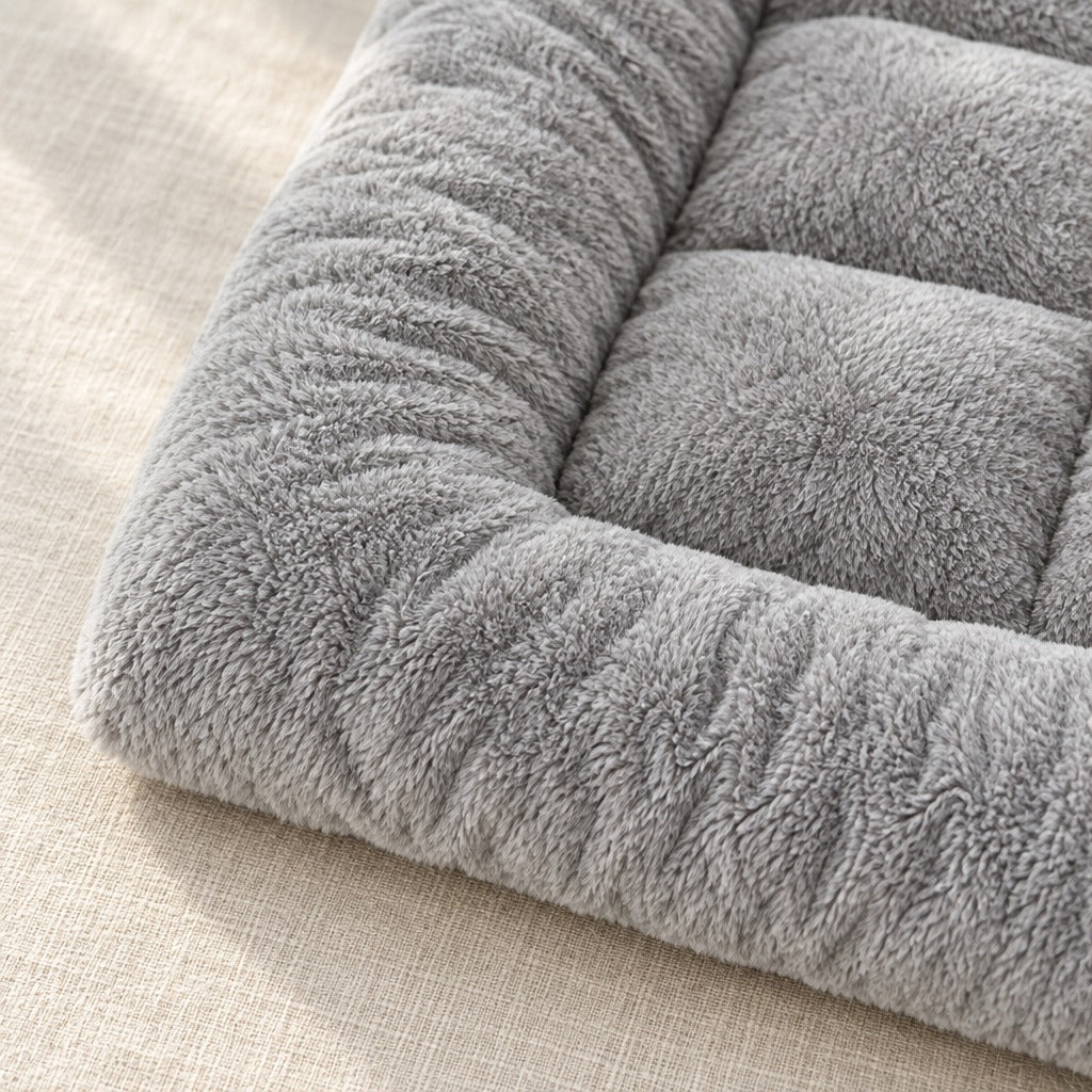 Gros plan sur un angle du tapis matelassé gris perle, la peluche à poil moyen et la couture du bourrelet rembourré.