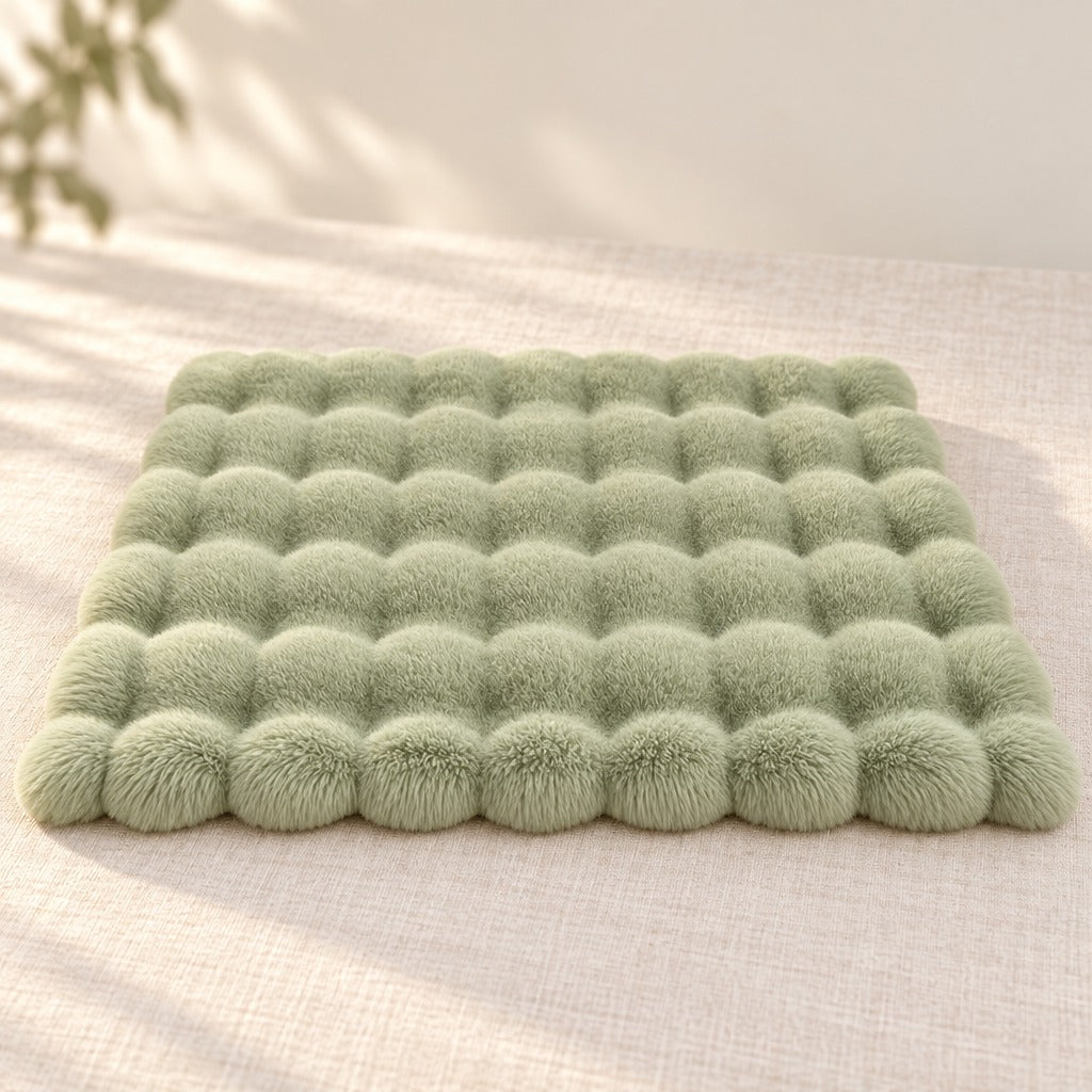 Le tapis vert sauge seul, posé à plat sur une toile de lin claire, vu de trois quarts.