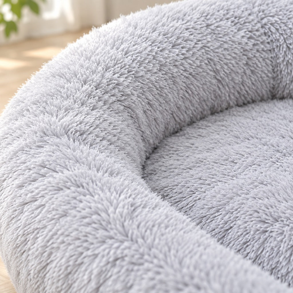 Gros plan sur la fourrure à poil long gris perle du couchage ovale pour chien, à la couture entre le bourrelet et le matelas intérieur.