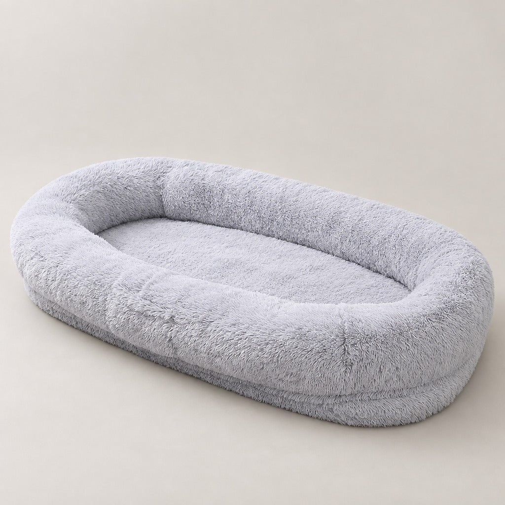 Le très grand couchage ovale pour chien en gris perle, vu seul de trois quarts sur fond clair, bourrelet continu et matelas intérieur plat.