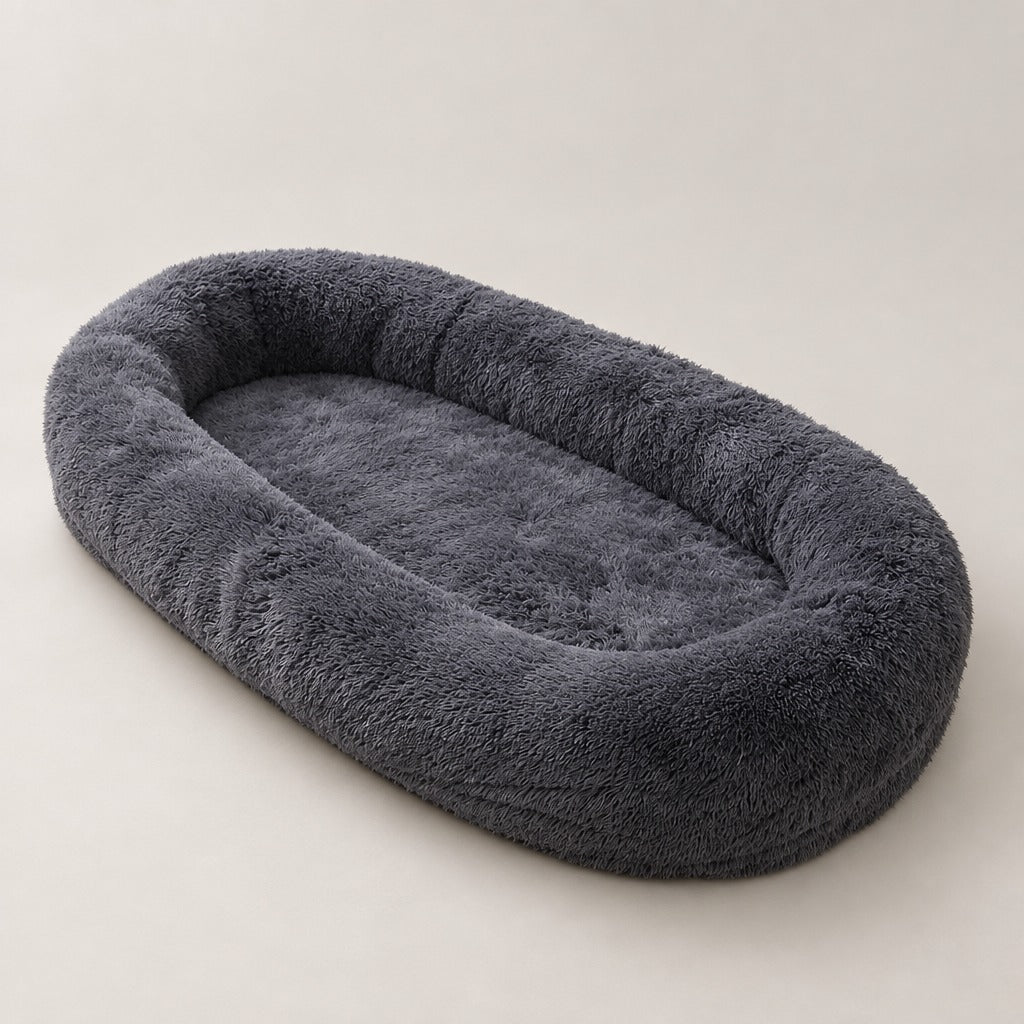 Le très grand couchage ovale pour chien en gris anthracite, vu seul de trois quarts sur fond clair, bourrelet continu tout autour.